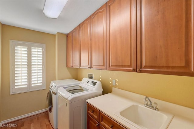 washroom with baseboards, a sink, independent washer and dryer, light wood finished floors, and cabinet space