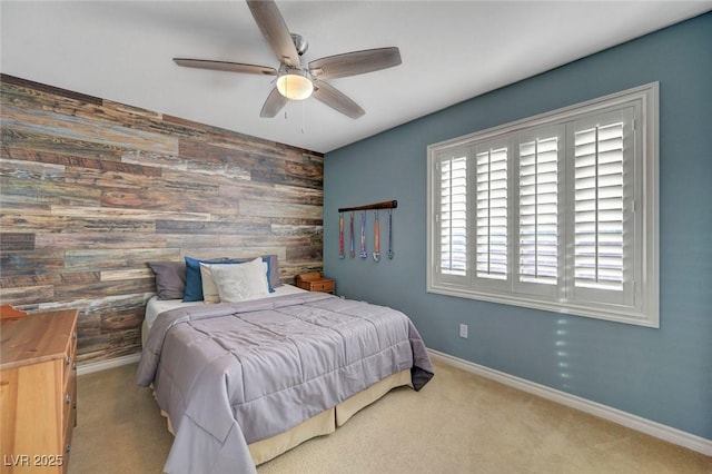 carpeted bedroom featuring wood walls, an accent wall, baseboards, and ceiling fan