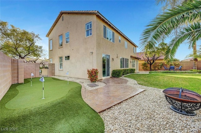 rear view of house featuring a fenced backyard, a fire pit, and stucco siding