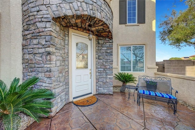 property entrance with a patio, fence, stucco siding, and stone siding
