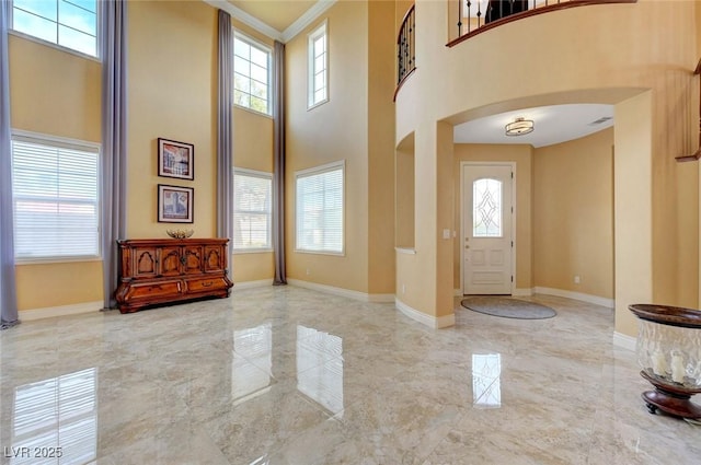entrance foyer with arched walkways, a high ceiling, marble finish floor, and baseboards