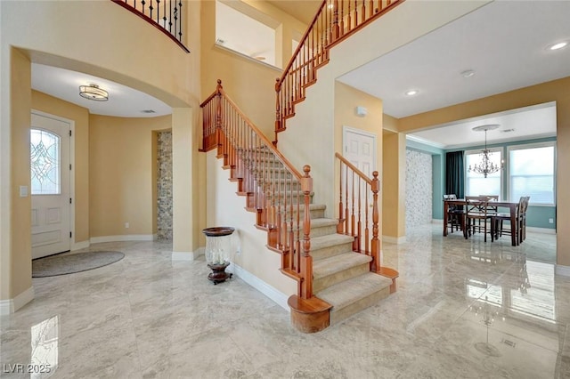 foyer entrance featuring stairs, a notable chandelier, marble finish floor, and baseboards