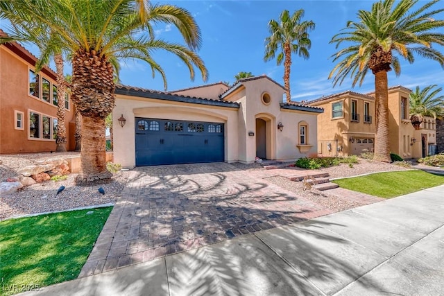 1045 Via Camelia St, Henderson, NV 89011 - mediterranean / spanish-style house with a tile roof, an attached garage, decorative driveway, and stucco siding
