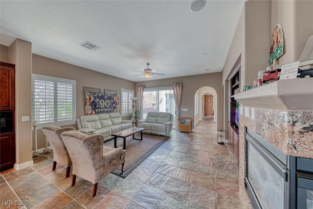 1045 Via Camelia St, Henderson, NV 89011 - living area with ceiling fan, arched walkways, stone tile floors, visible vents, and baseboards