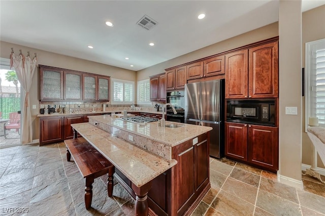 1045 Via Camelia St, Henderson, NV 89011 - kitchen featuring light stone counters, an island with sink, stone tile flooring, visible vents, and black appliances