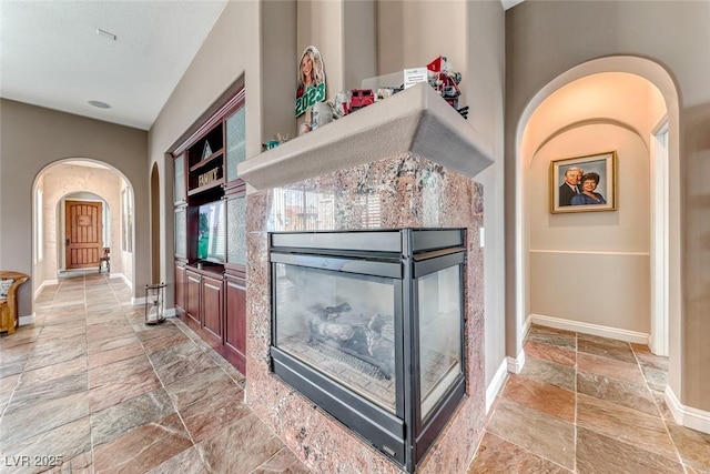 1045 Via Camelia St, Henderson, NV 89011 - living room featuring arched walkways, stone tile floors, baseboards, and a multi sided fireplace