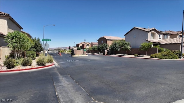 view of road featuring street lights, curbs, a gated entry, a gate, and a residential view