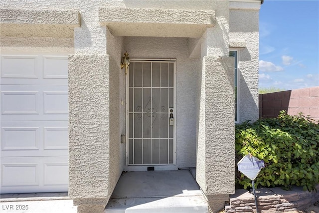 view of exterior entry with a garage and stucco siding