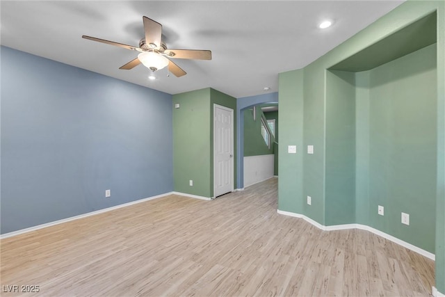 empty room featuring light wood-style flooring, ceiling fan, arched walkways, and baseboards