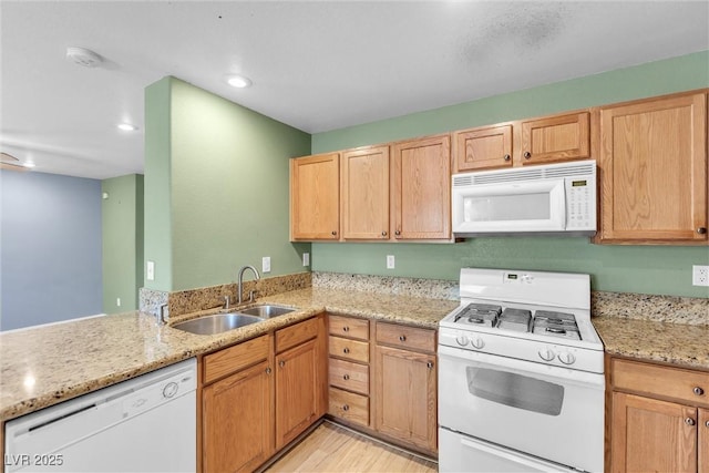 kitchen with light stone counters, light wood finished floors, a sink, and white appliances