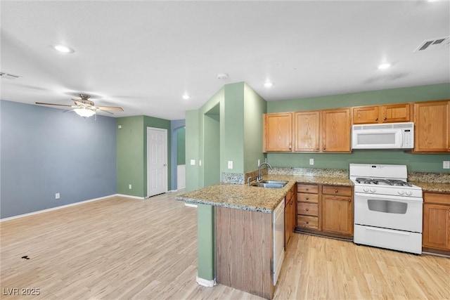 kitchen featuring white appliances, a peninsula, visible vents, a sink, and light wood finished floors