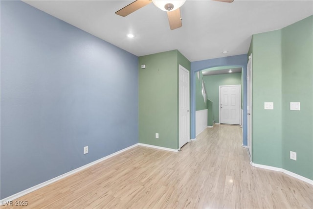spare room with arched walkways, wood finished floors, ceiling fan, and baseboards