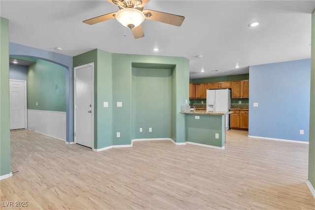 unfurnished living room featuring baseboards, recessed lighting, ceiling fan, arched walkways, and light wood finished floors