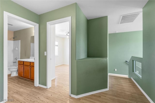 corridor with light wood-type flooring, a sink, baseboards, and visible vents