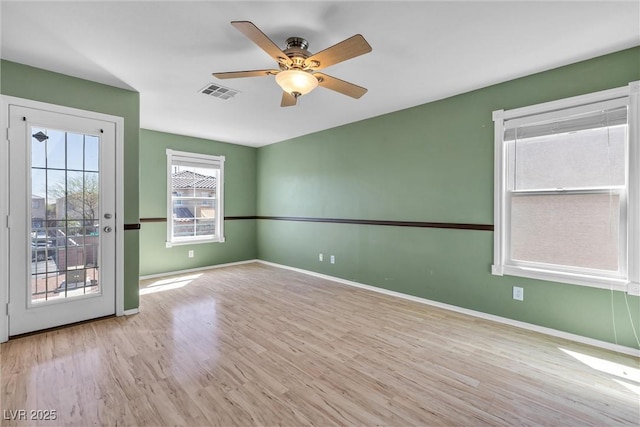 empty room with wood finished floors, ceiling fan, baseboards, and visible vents