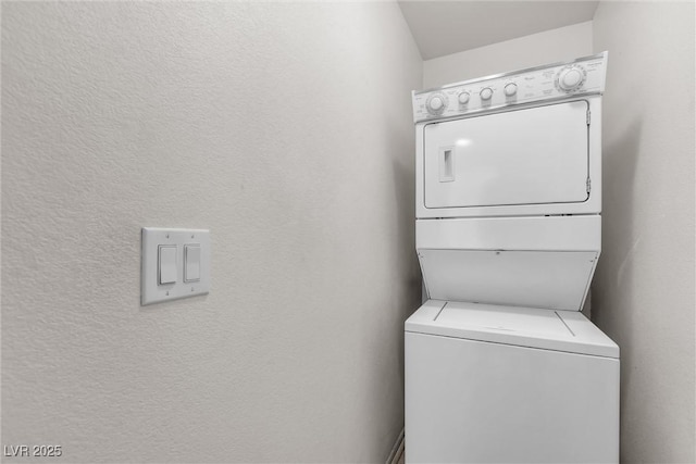 clothes washing area featuring a textured wall, stacked washer and dryer, and laundry area