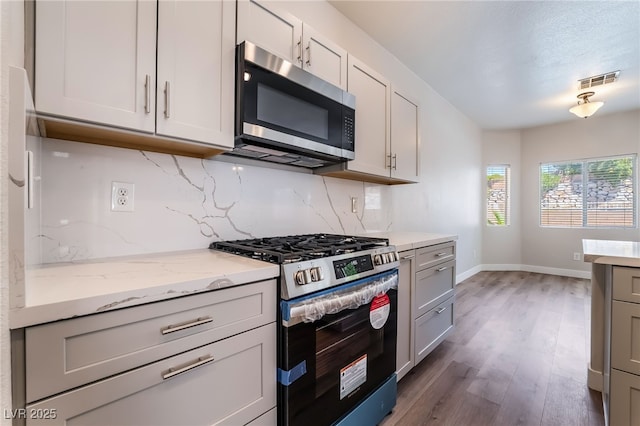 kitchen with stainless steel appliances, tasteful backsplash, baseboards, wood finished floors, and light stone counters