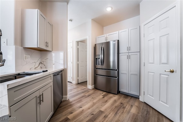 kitchen featuring appliances with stainless steel finishes, light wood-style flooring, tasteful backsplash, light stone counters, and a sink
