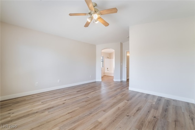 empty room with arched walkways, baseboards, a ceiling fan, and light wood-style floors