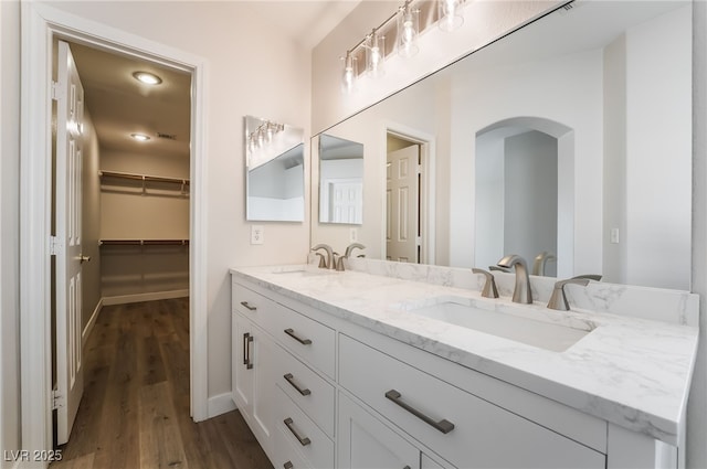 full bath with wood finished floors, double vanity, a walk in closet, and baseboards