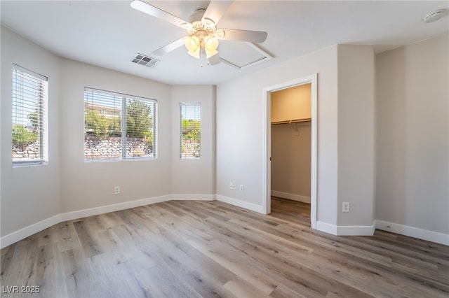 unfurnished bedroom with light wood-type flooring, a spacious closet, ceiling fan, and baseboards