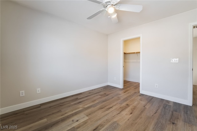 unfurnished bedroom with baseboards, wood finished floors, a spacious closet, a closet, and a ceiling fan