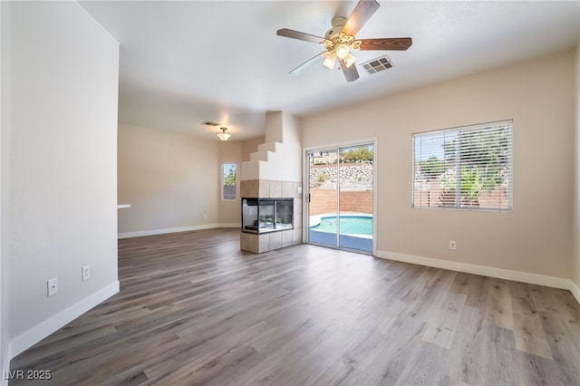 unfurnished living room with wood finished floors, a ceiling fan, baseboards, and a tiled fireplace