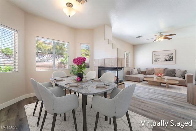 dining area featuring wood finished floors, baseboards, a tile fireplace, and ceiling fan