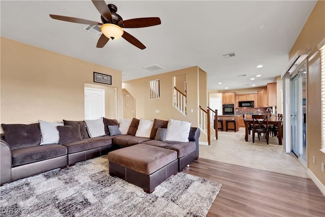 living area with visible vents, ceiling fan, light wood finished floors, and stairs