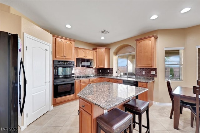 kitchen with a sink, tasteful backsplash, black appliances, and light stone countertops