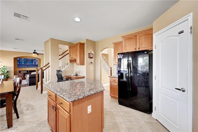 kitchen featuring light tile patterned flooring, black fridge with ice dispenser, light stone countertops, visible vents, and arched walkways