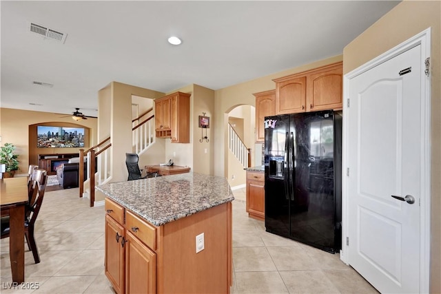 kitchen featuring light tile patterned floors, arched walkways, black fridge, and light stone counters