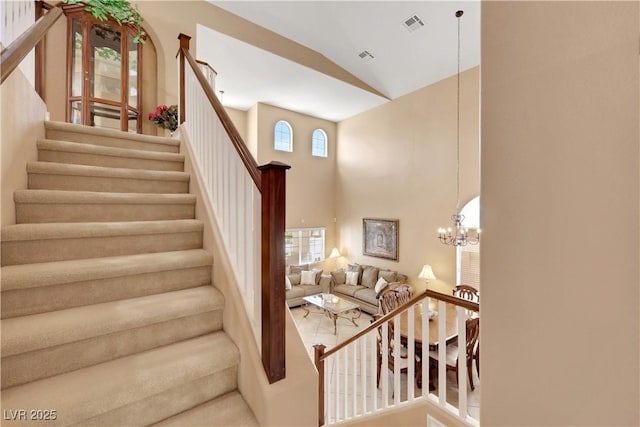 staircase featuring high vaulted ceiling, visible vents, and a chandelier