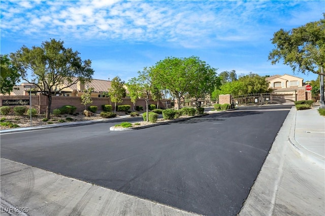 view of road with a residential view, traffic signs, curbs, a gate, and sidewalks