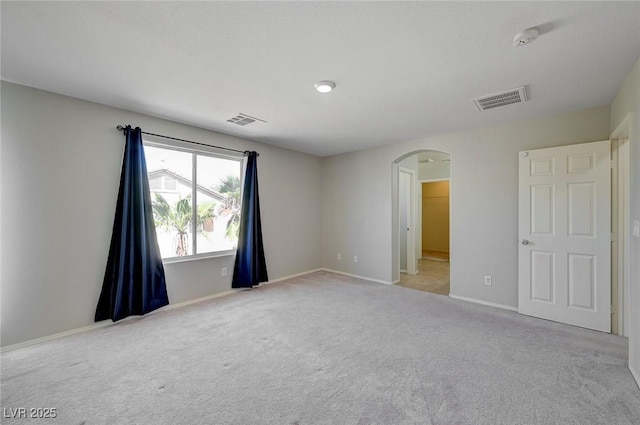 carpeted spare room featuring arched walkways, visible vents, and baseboards