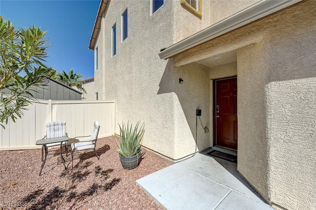 property entrance with fence, a patio, and stucco siding
