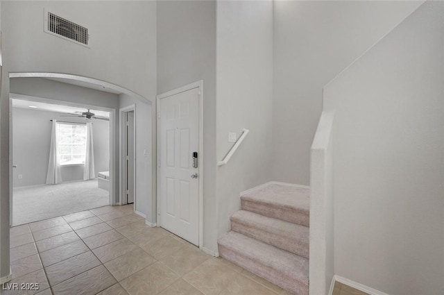 stairs with visible vents, baseboards, arched walkways, a ceiling fan, and a towering ceiling