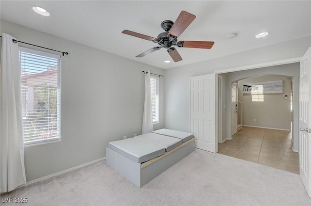 unfurnished bedroom featuring light carpet, arched walkways, multiple windows, and baseboards