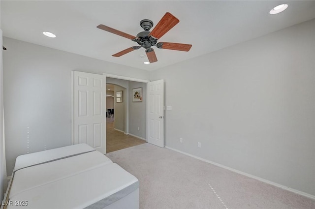 unfurnished bedroom featuring ceiling fan, arched walkways, light colored carpet, recessed lighting, and baseboards