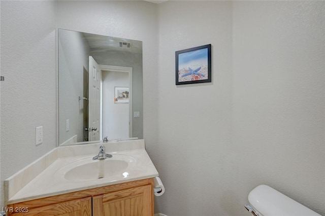 bathroom with toilet, vanity, a textured wall, and visible vents