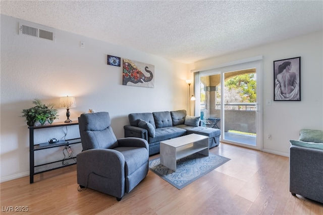 living room with a textured ceiling, visible vents, baseboards, and light wood-style floors