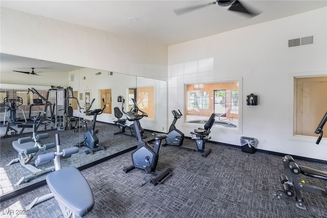 gym with carpet flooring, ceiling fan, visible vents, baseboards, and a towering ceiling