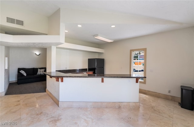 kitchen featuring recessed lighting, freestanding refrigerator, baseboards, visible vents, and a kitchen breakfast bar