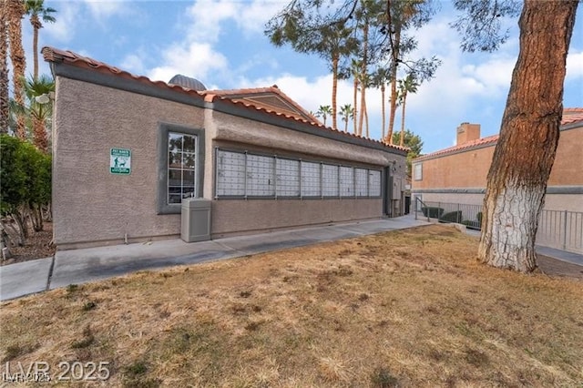 view of property exterior featuring stucco siding, fence, a tiled roof, and mail area
