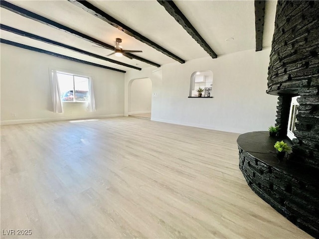 unfurnished living room with arched walkways, wood finished floors, baseboards, and a ceiling fan