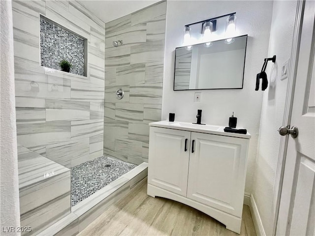 full bath featuring a tile shower, vanity, and wood finished floors