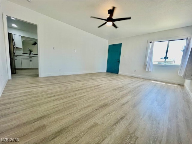 unfurnished bedroom with baseboards, a sink, light wood-type flooring, and black fridge