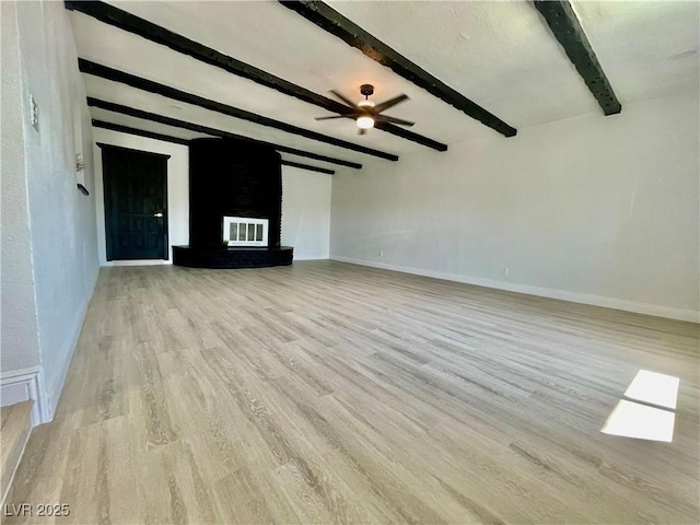 unfurnished living room with baseboards, ceiling fan, a fireplace, beam ceiling, and light wood-style flooring