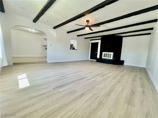unfurnished living room with baseboards, light wood-style flooring, a ceiling fan, beam ceiling, and arched walkways