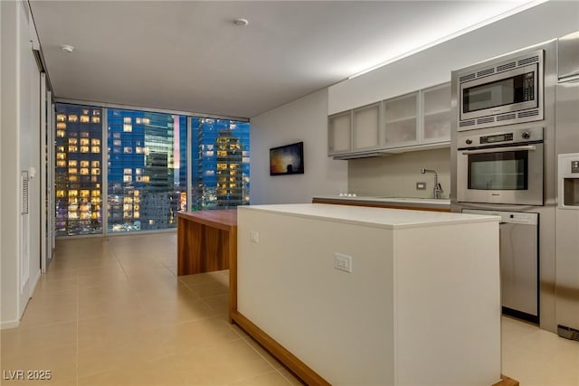 kitchen featuring light tile patterned floors, a center island, appliances with stainless steel finishes, light countertops, and a sink
